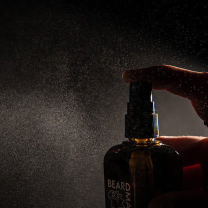 Hand holding a bottle labeled 'BEARDMATE' and sprays on a dark background